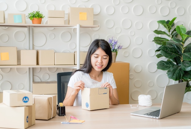 Asian woman business owner working at home with packing box on workplace