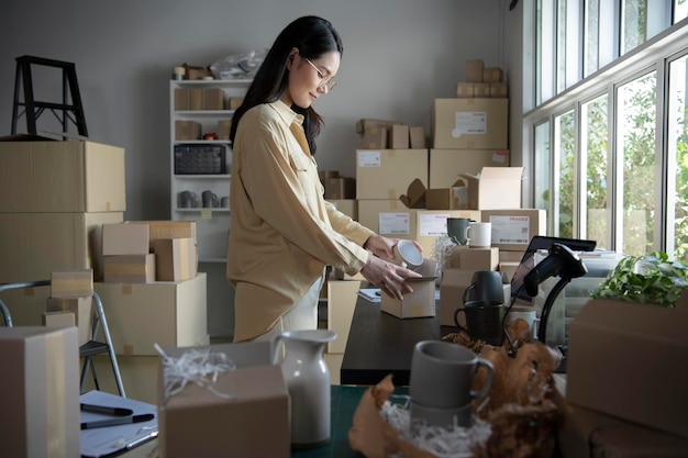 Asian woman business owner working packing the order for shipping to customer Female entrepreneur packaging box for delivery in store warehouse