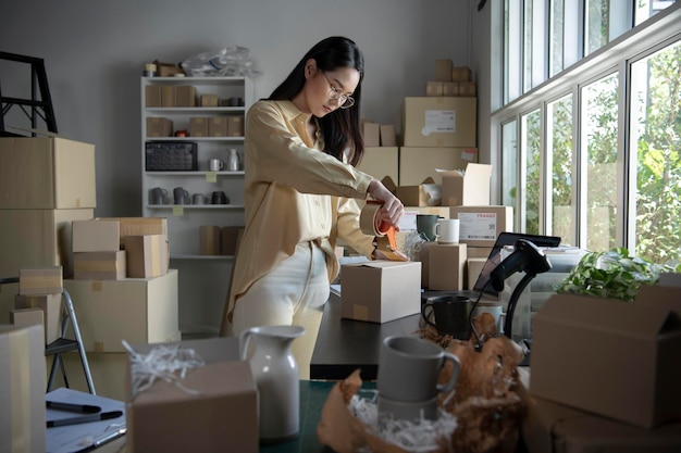 Asian woman business owner working packing the order for shipping to customer Female entrepreneur packaging box for delivery in store warehouse