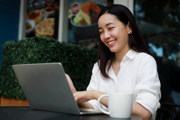 Foto donna asiatica ad un caffè che lavora ad un computer portatile