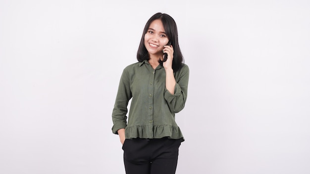 Asian woman calling and smiles standing on white wall