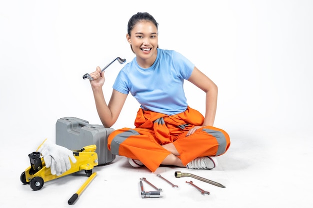 Asian woman car technician in uniform sitting with a car jack and toolkit box and wrench