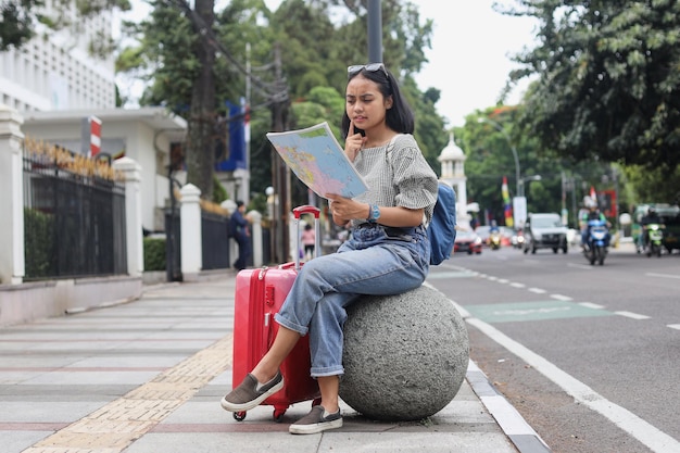 Asian woman in casual style bring luggage reading map think about direction to next destination