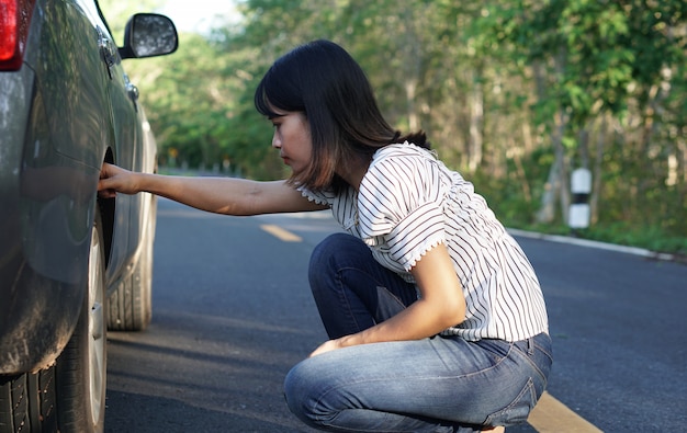 アジアの女性森の周りの道路で壊れた車をチェックします。