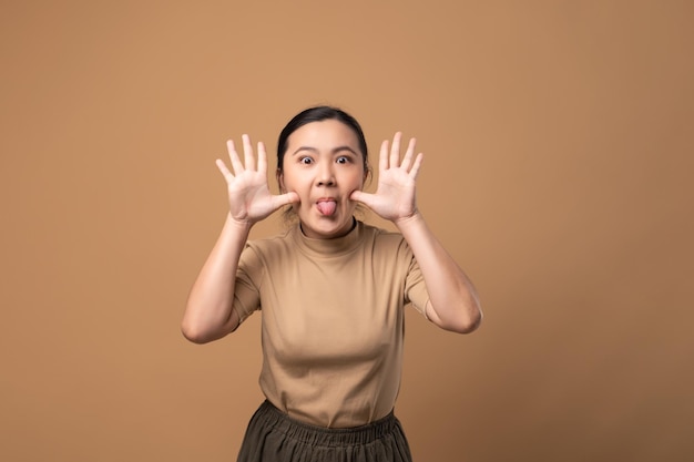 Donna asiatica che gioca allegra sbircia un fischio con le mani che mostrano il viso in piedi isolato su sfondo beige
