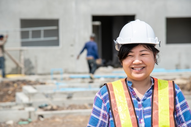 写真 建物や建設現場で幸せに働くヘルメットと安全ベストを持つアジアの女性土木建設エンジニアの労働者または建築家