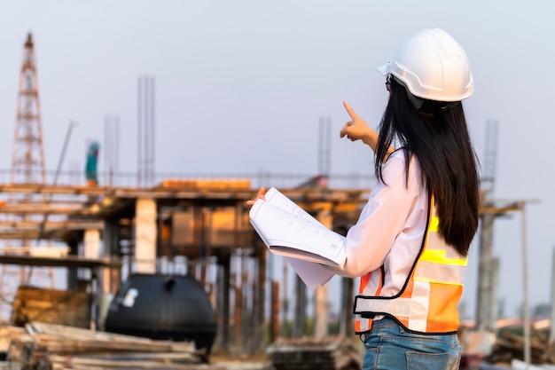 Asian woman civil engineer paper plan building architect wearing white safety helmet