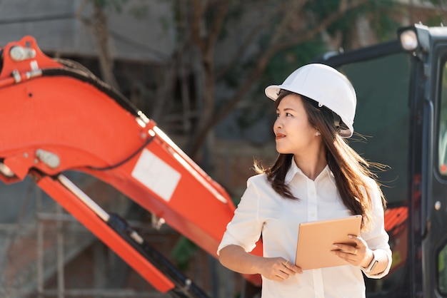 白い安全ヘルメットを持つアジア女性土木技師が工事現場を訪問します。