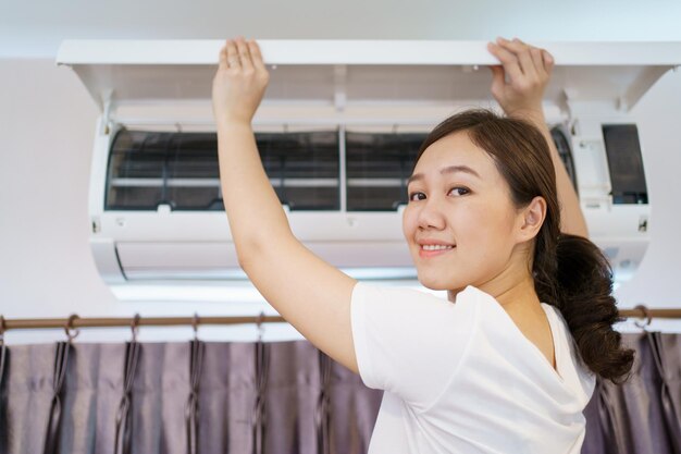 Asian woman cleaning a dirty and dusty air conditioning filter\
in her house housewife removing a dusty air conditioner filter