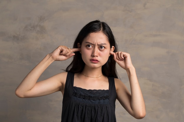 아시아 여자는 무언가를 듣지 않는 손으로 귀를 닫습니다.