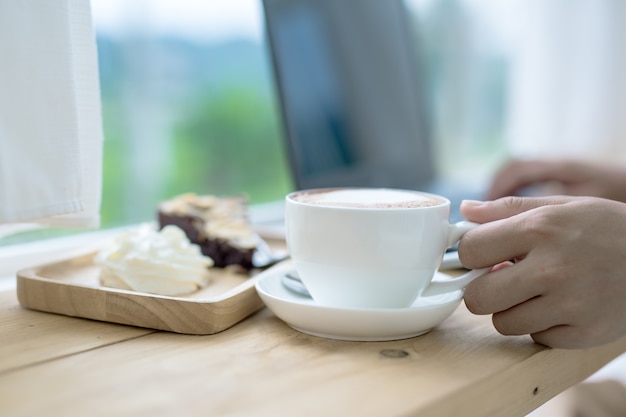 コーヒーショップでラップトップで作業するためのアジアの女性のコーヒー。