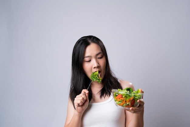 Donna asiatica confusa con il mangiare insalata isolata sopra il muro bianco. stile di vita sano con il concetto di cibo pulito.