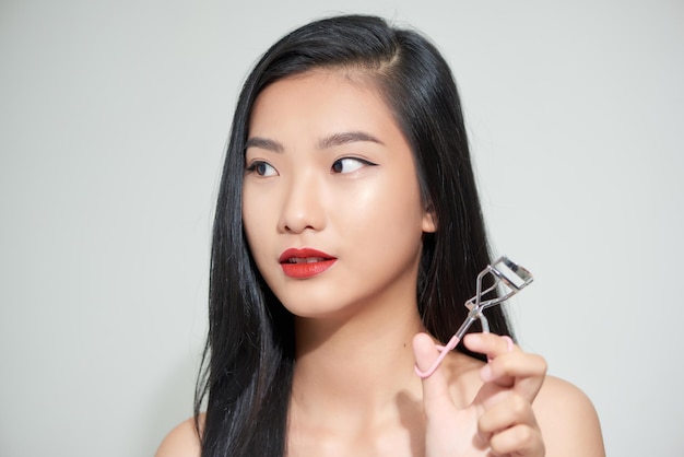 Photo asian woman corrects eyelashes with curling tongs close up