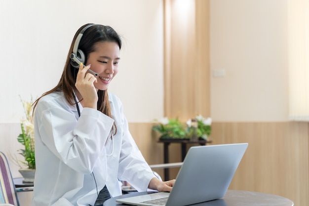 Asian woman doctor in headset taking calling on her headset microphone online for a ache patient