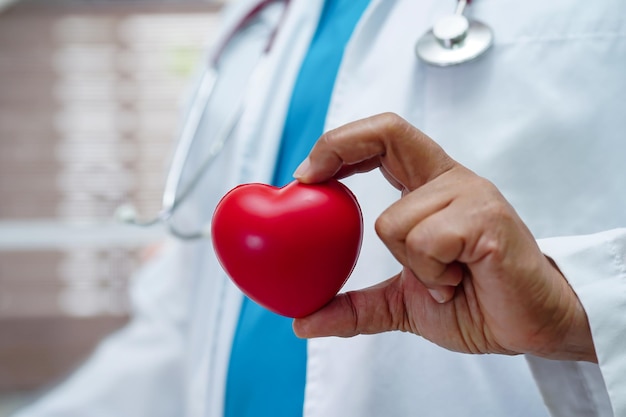 Asian woman doctor holding red heart for health in\
hospital