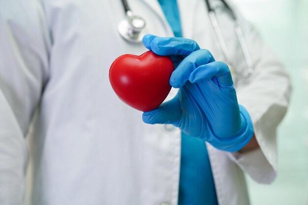 Asian woman doctor holding red heart for health in\
hospital