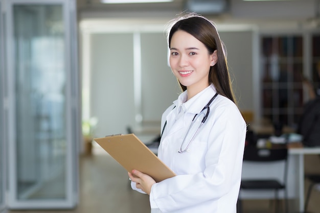 Asian woman doctor is smiling and standing confidently while she holds the document clipboard in her hands.