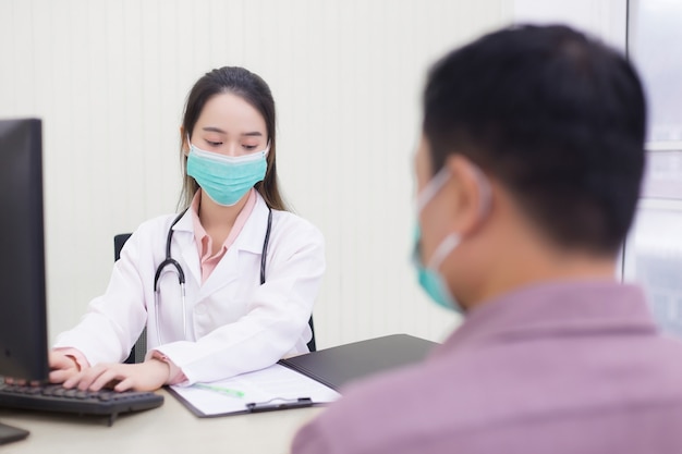 Asian woman doctor is typing on keyboard to record information into computer after talking about health of patient in hospital.