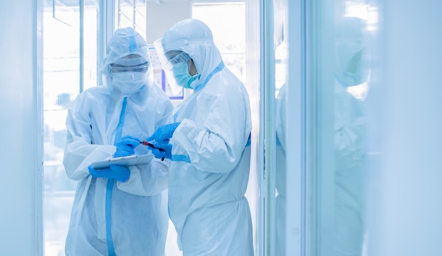 Asian woman doctor in personal protective suit with mask writing on quarantine patient chart, holding test tube with blood sample for screening coronavirus. Coronavirus, covid-19 concept.