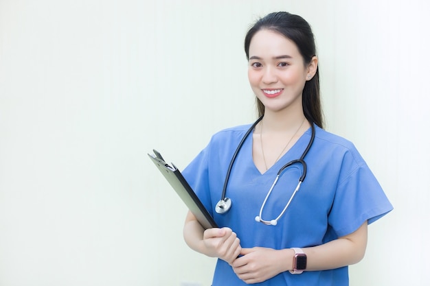 asian woman doctor standing smiling in a blue lab shirtholding patient documents in hand