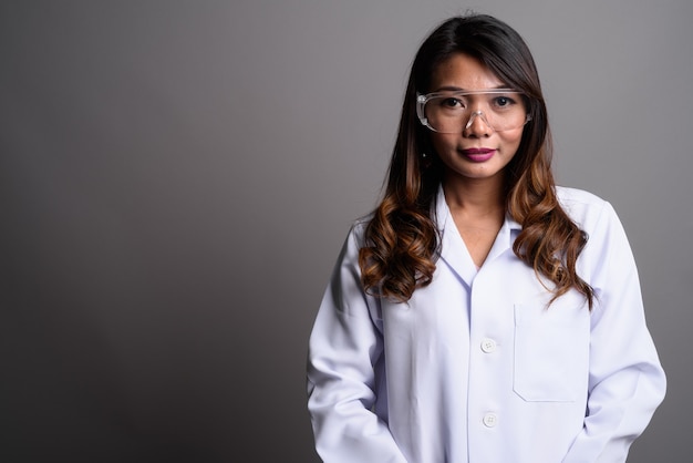 Asian woman doctor wearing protective glasses against gray backg