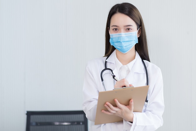 Asian woman doctor wears medical face mask and records the symptom of her patient on clipboard