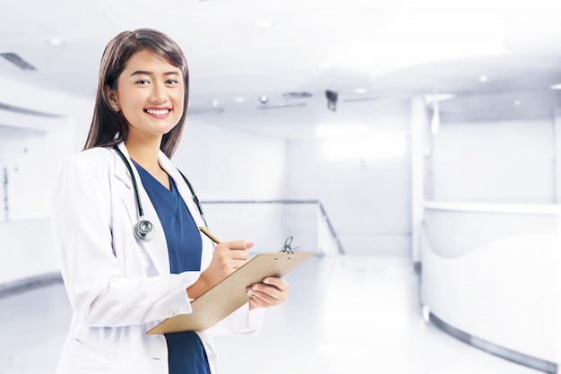 Asian woman doctor in white lab coat and stethoscope holding clipboard