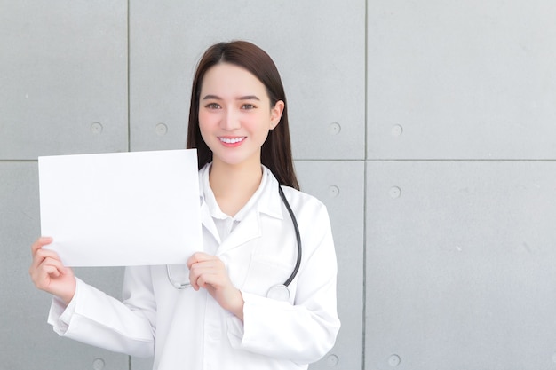 Asian woman doctor who wears medical coat holds and shows white paper to present something