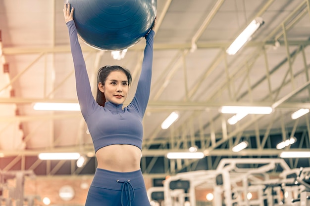 Foto donna asiatica che fa esercizio sulla palla fitness in palestra