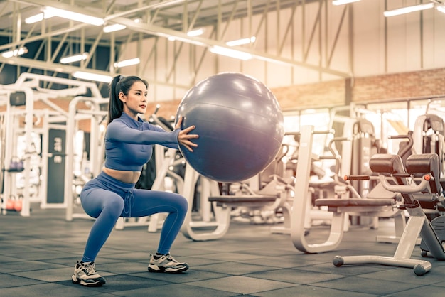 Foto donna asiatica che fa esercizio sulla palla fitness in palestra