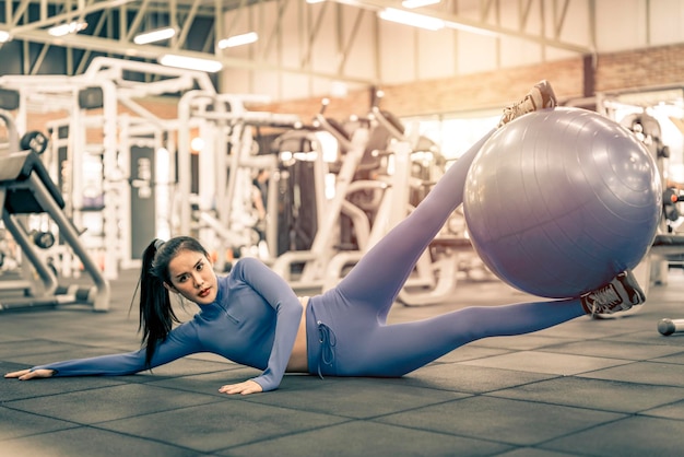 Foto donna asiatica che fa esercizio sulla palla fitness in palestra