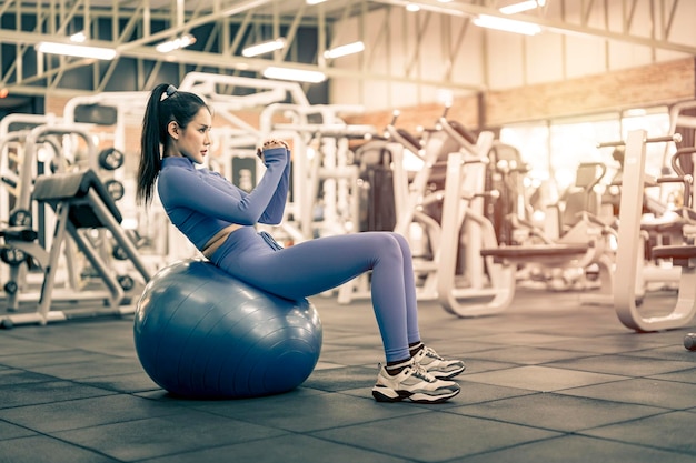 Donna asiatica che fa esercizio sulla palla fitness in palestra