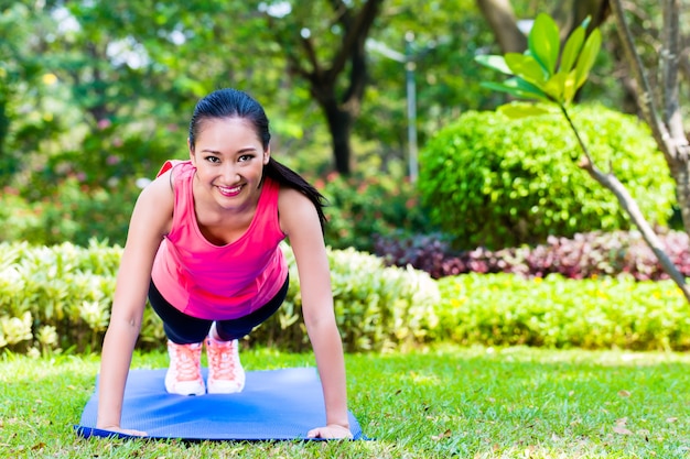 Asian woman doing push-ups in park