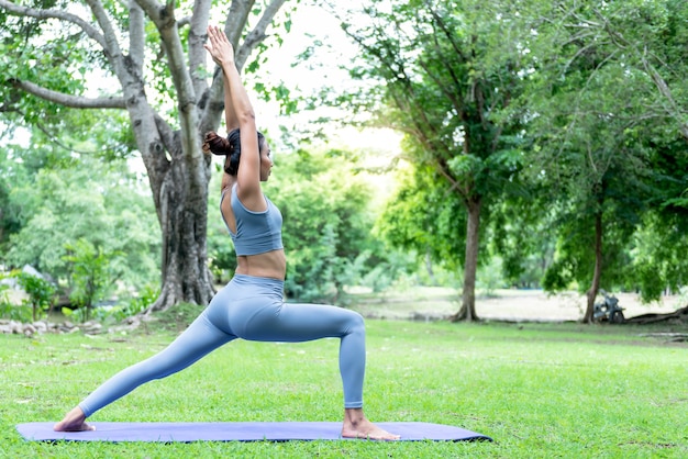 Donna asiatica che fa yoga in una postura elegante, nel verde del parco