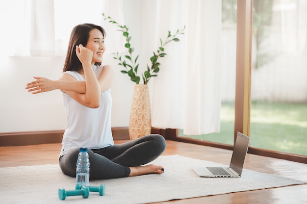 Donna asiatica che fa la spalla di yoga che allunga classe online a casa