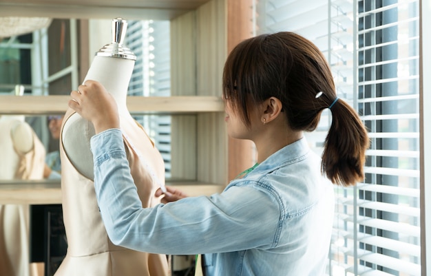 Asian woman dressmaker fashion designer measuring size of mannequin in showroom.