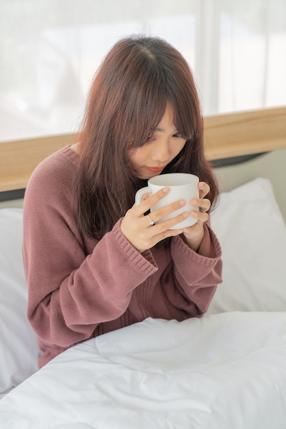 Asian woman drinking coffee on bed in the morning