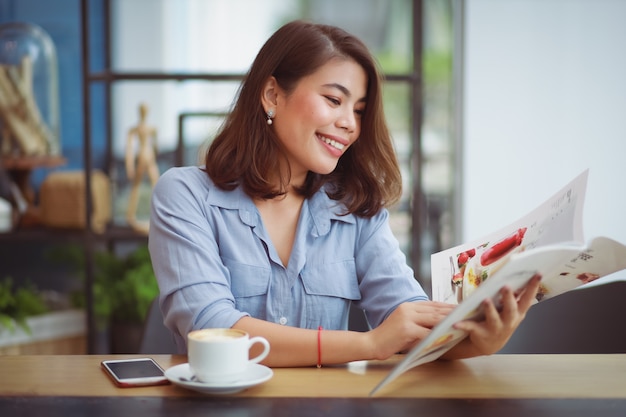 コーヒーショップカフェでコーヒーを飲みながら携帯電話を使用してアジアの女性