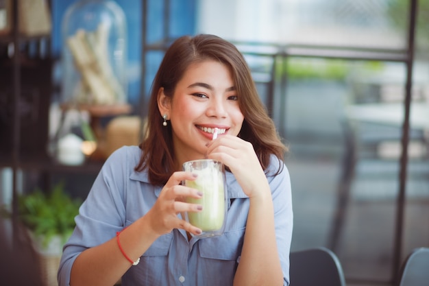 Foto caffè bevente della donna asiatica nel caffè della caffetteria e per mezzo del telefono cellulare