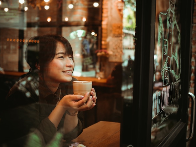 アジアの女性がコーヒーショップカフェでコーヒーを飲む