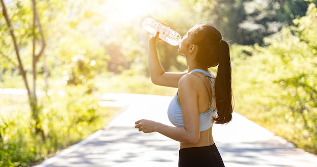조깅 후 물을 마시고 있는 아시아 여성, 그녀는 아침저녁으로 많은 사람들이 조깅을 하러 오는 공원에서 달리기를 하고 있어 달리기가 인기 있는 활동이다. 조깅과 건강 관리 개념입니다.