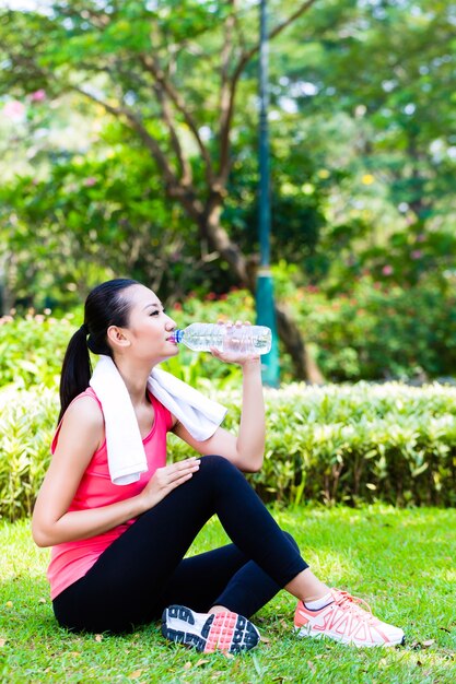 公園でスポーツの後に水を飲むアジアの女性