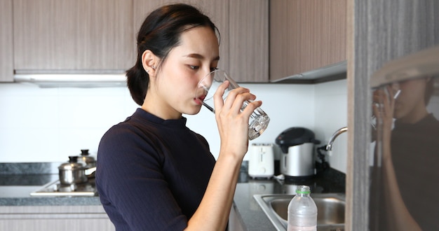 Acqua potabile della donna asiatica sul vetro in cucina