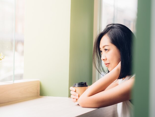 アジアの女性は暖かい光でカフェでホットコーヒーを飲みます。