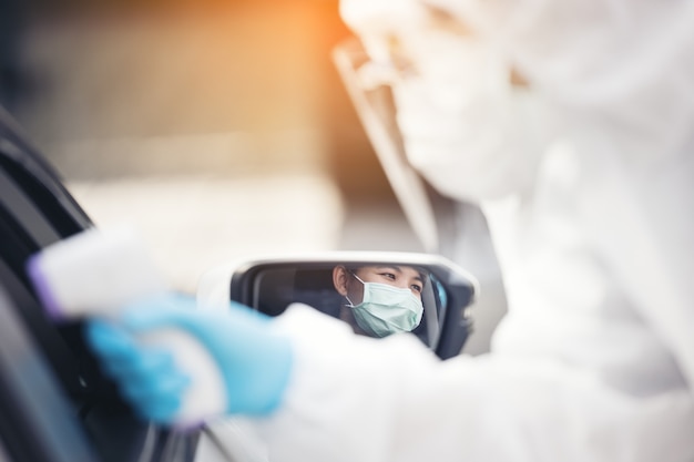 Asian woman drive thru covid-19 testing with ppe medical staff, covid test temp while check in cars