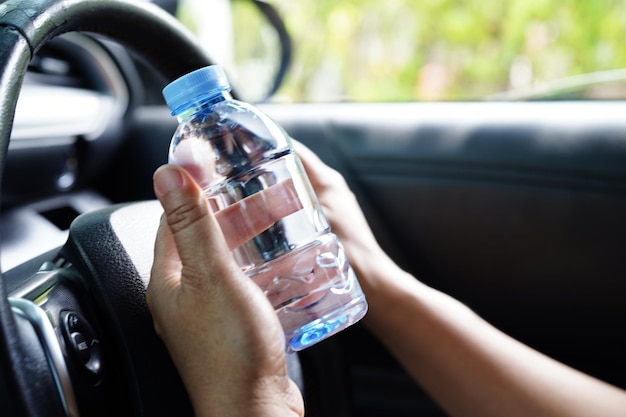 Asian woman driver hold cold water for drink in car dangerous and risk an accident