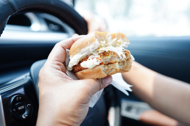 Asian woman driver hold and eat hamburger in car dangerous and risk an accident