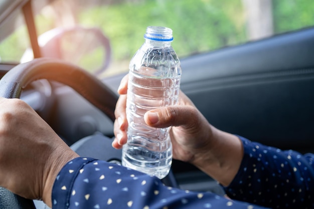 車の運転中に飲料水用のボトルを保持しているアジアの女性ドライバープラスチック湯たんぽが火災を引き起こす