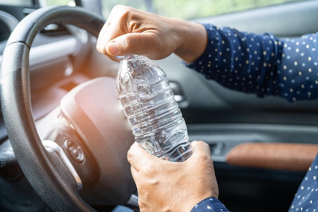 Autista donna asiatica che tiene una bottiglia per bere acqua durante la guida di un'auto la bottiglia di plastica dell'acqua calda provoca incendi