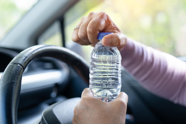 車の運転中に飲料水用のボトルを保持しているアジアの女性ドライバープラスチック湯たんぽが火災を引き起こす